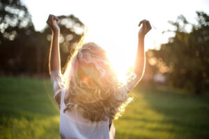 Image of woman facing the sun with her hands in the air